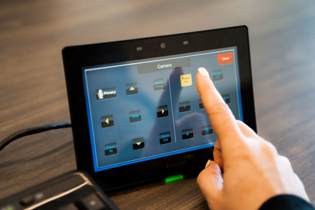 Closeup of a finger pressing a button on an AV control system screen